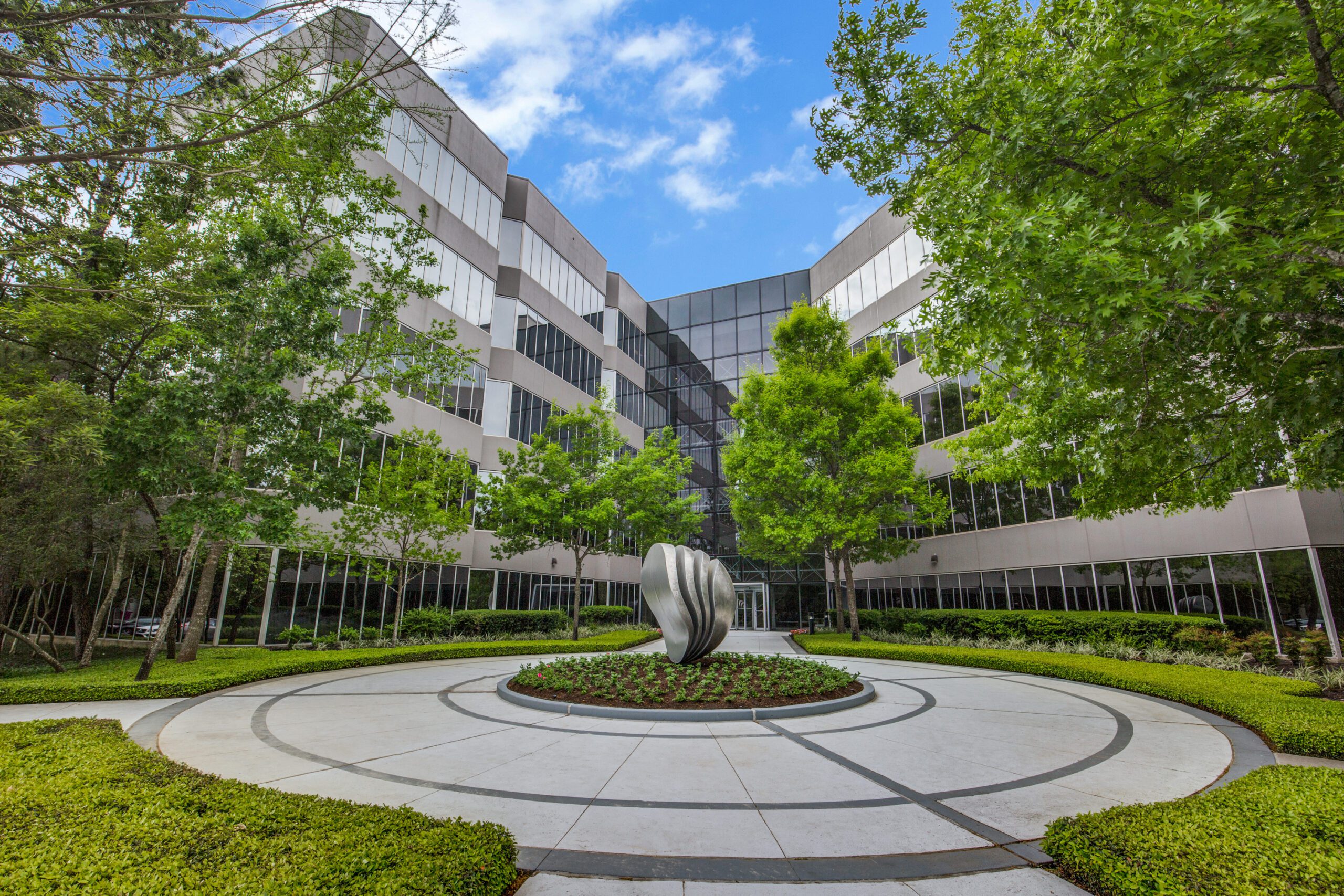 Front entrance to office building with circular fountain, surrounded by lush greenery.